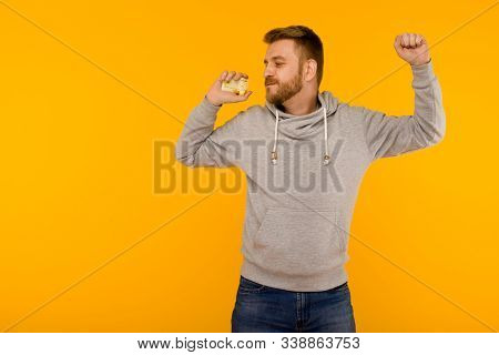 Attractive Man In A Gray Sweatshirt Joyfully Dances With A Credit Card In His Hand On A Yellow Backg