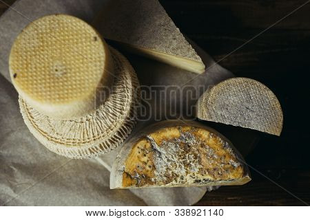 Different Homemade Cheeses On A Dark Wooden Background. Pieces And Cheese Heads Of Gorgonzola, Asiag