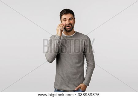 Carefree Enthusiastic, Bearded Male In Grey Sweater Talking On Phone With Pleased, Happy Smile, Hold