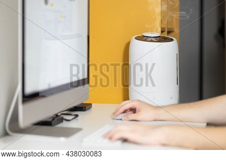 White Air Humidifier Spreading Steam Up. Humidification Of Dry Air While Man Working On Computer. Se