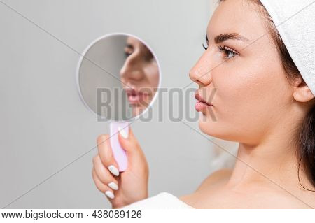Rhinoplasty. A Young Beautiful Woman Holds A Mirror With Aquiline Nose. Comparison Of Results Before