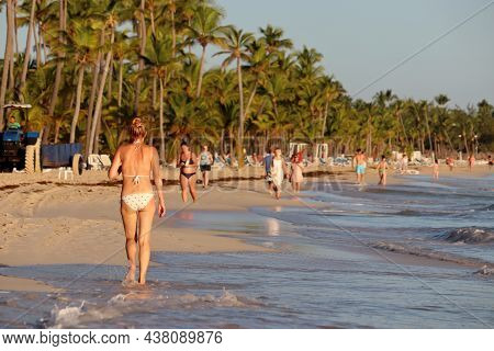 People Walking By The Sand Of Tropical Beach, Woman In Bikini In Foreground. View To Coconut Palm Tr