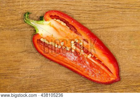 Half Of The Fresh Red Bell Pepper Cut Lengthwise Lies On The Wooden Cutting Board, Top View