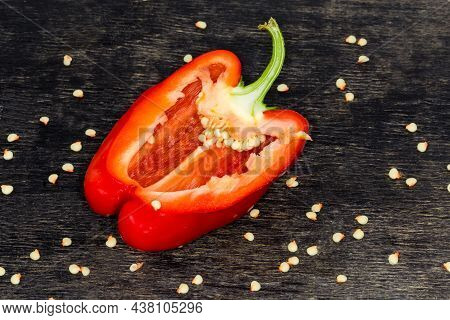 Half Of The Fresh Red Bell Pepper Cut Lengthwise Lies On The Dark Surface Among The Scattered Pepper