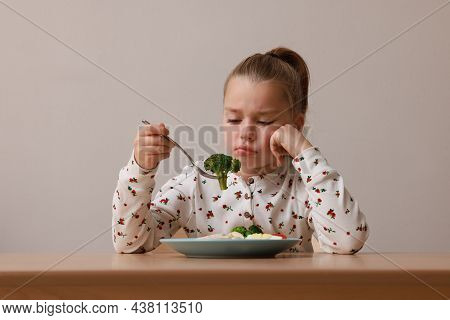 Cute Little Girl Refusing To Eat Her Dinner At Table On Grey Background
