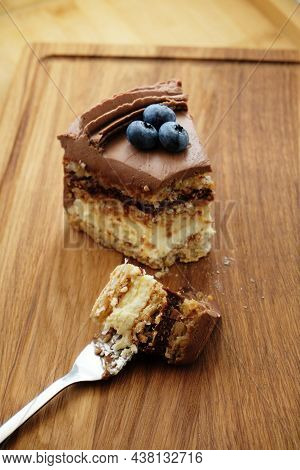 Piece Of Kiev Cake With Chocolate Icing And Blueberries On Wooden Board. A Bite Of Cake On A Fork