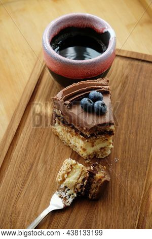Piece Of Kiev Cake With Chocolate Icing And Blueberries And Cup Of Coffee On Wooden Board. A Bite Of