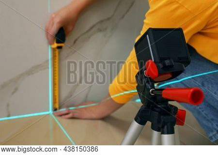 Woman Using Cross Line Laser Level And Tape For Accurate Measurement On Tiled Wall, Closeup