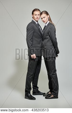 Fashion shoot. Full length portrait of stylish young man and woman in elegant striped pantsuits on a gray background. Impeccable look. Men's clothing style. 