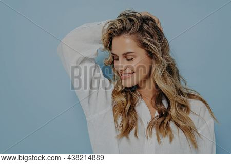 Relaxed Romantic Blonde Woman With Long Wavy Hair And Hand Behind Her Head, Looking Down With Bright