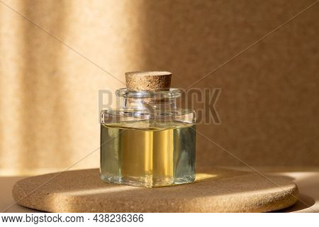 Square Bottle With Cosmetic Oil On Round Wooden Stand, In Rays Of Sunlight. Monochrome Beige Backgro