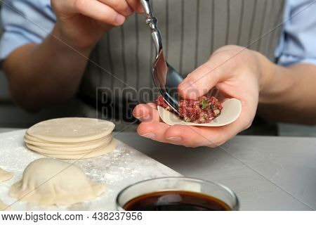 Woman Putting Gyoza Filling In Center Of Dough Wrapper At Light Grey Table, Closeup