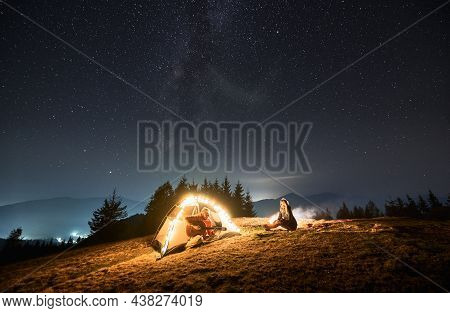 Man Sitting In Brightly Lit Tent In The Middle Of Mountain Hill At Night, Playing At Favorite Guitar