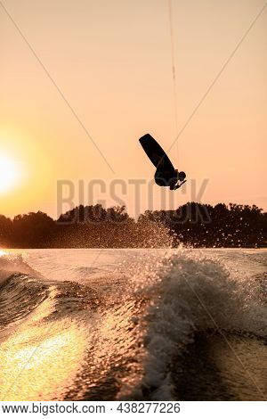 Dark Silhouette Of Man Holding Rope And Making Jump On Wakeboard At Sunset.