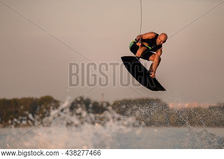 Active Muscular Man Making Trick And Jump With Wakeboard On Sky Background.