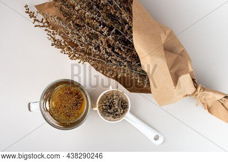 Glass Of Herb Tea, Tea Strainer And Wormwood Twigs Wrapped In Brown Paper.