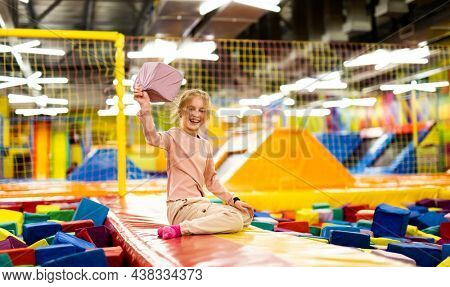 Pretty girl kid sitting on colorful trampoline at playground park and holding gum cube. Beautiful female child happy during active entertaiments indoor