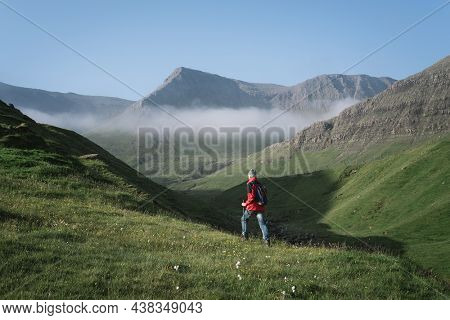 Hiker walks on the buttercup route between Bour and Gasadalur, Faroe Islands
