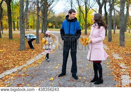 Family resting in the autumn park along the path. Beautiful nature and trees with yellowleaves.