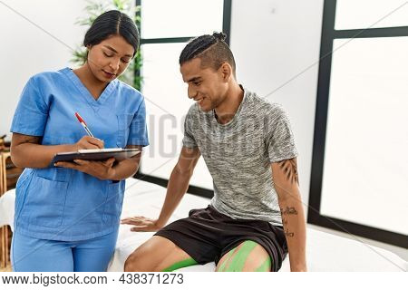 Young latin physioterapist woman asking to patient at the clinic.