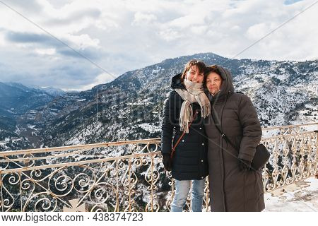 Winter Portrait Of Hugging And Smiling Mother And Daughter With Splendid Snow-covered Mountains View