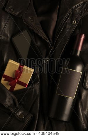 Wine bottle, present and cell phone on a leather bomber jacket. Flat lay with copy space.