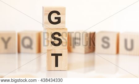 Wooden Cubes With Letters Gst Arranged In A Vertical Pyramid, On The Light Background, Reflection Su