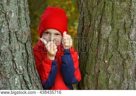 A Little Boy Smiles And Shows Class While Standing Between The Trees