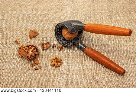 Nutcracker With Broken Tasty Walnuts On Burlap. One Nut In A Nutcracker.