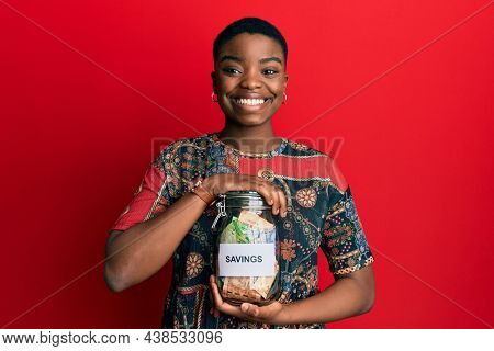 Young african american woman holding savings jar with south african rands money smiling with a happy and cool smile on face. showing teeth. 
