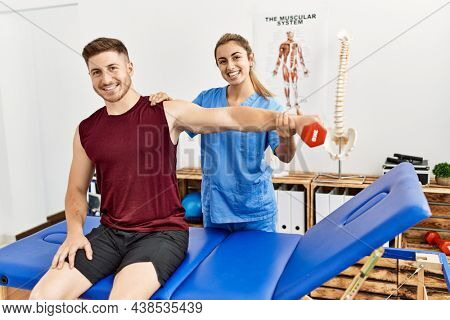 Young hispanic physioterapist woman make arm rehab treatment to man at the clinic.