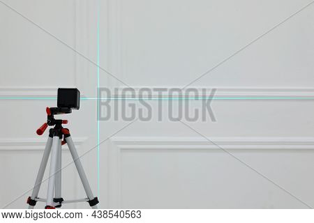 Cross Line Laser Level On Tripod In Front Of White Wall