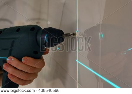 Woman Using Cross Line Laser Level For Accurate Measurement And Driving Screw In Tiled Wall, Closeup