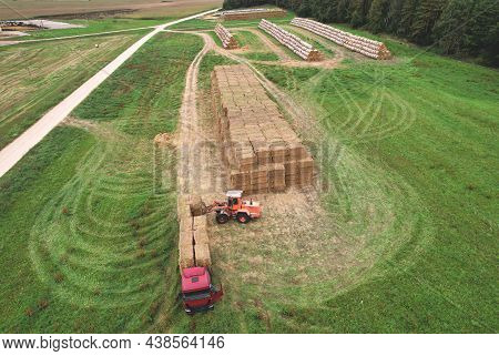Farmer Unloading Round Bales Of Straw From Hay Trailer With A Front End Loader. Store Hay At Farm. H