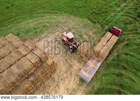 Farmer Unloading Round Bales Of Straw From Hay Trailer With A Front End Loader. Store Hay At Farm. H