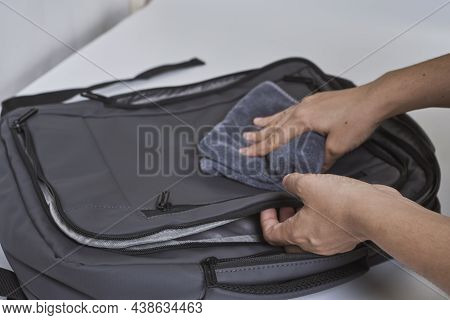 Cleaning Backpack With Washcloth. A Person Wipes Off Dirt Or Dust From The Outside Of The Bag. Wipin