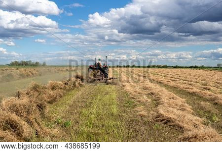 Rear View Of Tractor Collecting Hay With Old Wheel Rake In Field In Spring