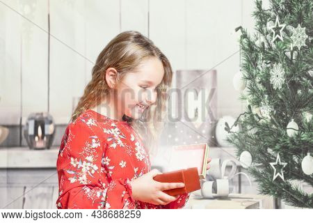 Little Girl At Home In Red Dress Opening Gift Box At Christmas