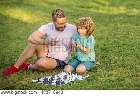 Tutorship. Daddy And Child Play Logic Game. Father And Son Playing Chess On Grass In Park.