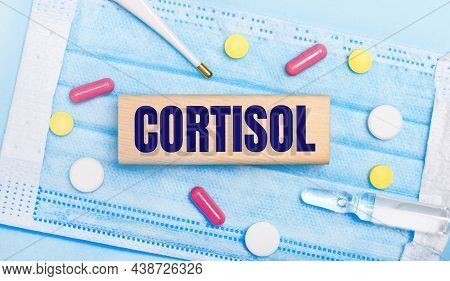 On A Light Blue Disposable Face Mask There Are Tablets, A Thermometer, An Ampoule And A Wooden Block