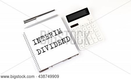 Notepad With Text Interim Dividend With Calculator And Pen. White Background. Business