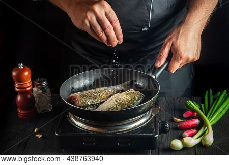 Professional Chef Prepares Fresh Fish In Pan Sprinkling Salt With Ingredients. Preparing To Cook Fis
