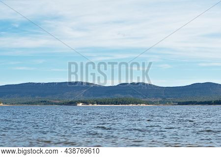 Waters Of The Cuerda Del Pozo Reservoir. In The Background Pine Forests And Rocky Mountains. Cloudy 