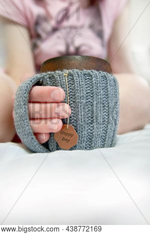 Cozy Morning In Bed With Glanny Mug Of Coffee, Womens Hands Hold A Mug In Knitted Cover. Close-up.