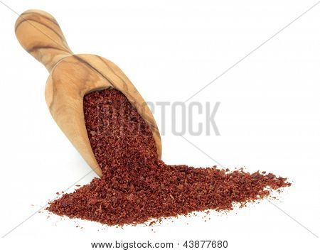 Especia de zumaque en una cuchara de madera olivo sobre fondo blanco.