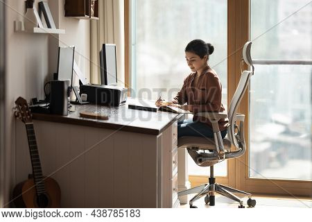 Serious Indian Female Sit At Desk Holds Pen Jotting Information