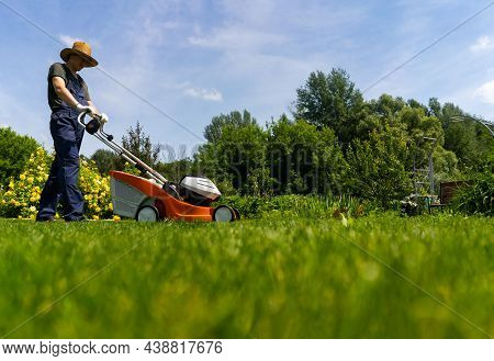 A Young Man In A Straw Hat Is Mowing A Lawn With A Lawn Mower In His Beautiful Green Floral Summer G