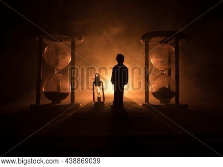 Time Concept. Silhouette Of Hourglass Clock And Old Vintage Wood Clock With Arrow And Smoke On Dark