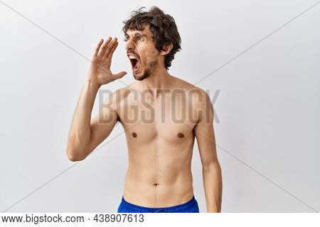 Young hispanic man standing shirtless over isolated, background shouting and screaming loud to side with hand on mouth. communication concept. 