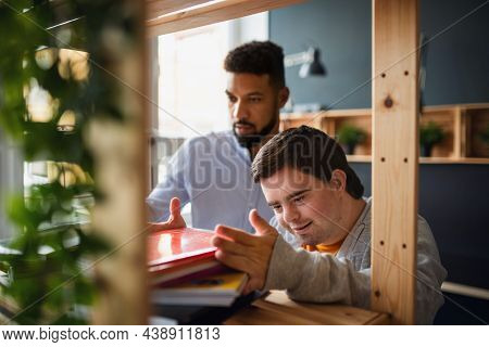 Young Happy Man With Down Syndrome And His Tutor Indoors At Staffroom.